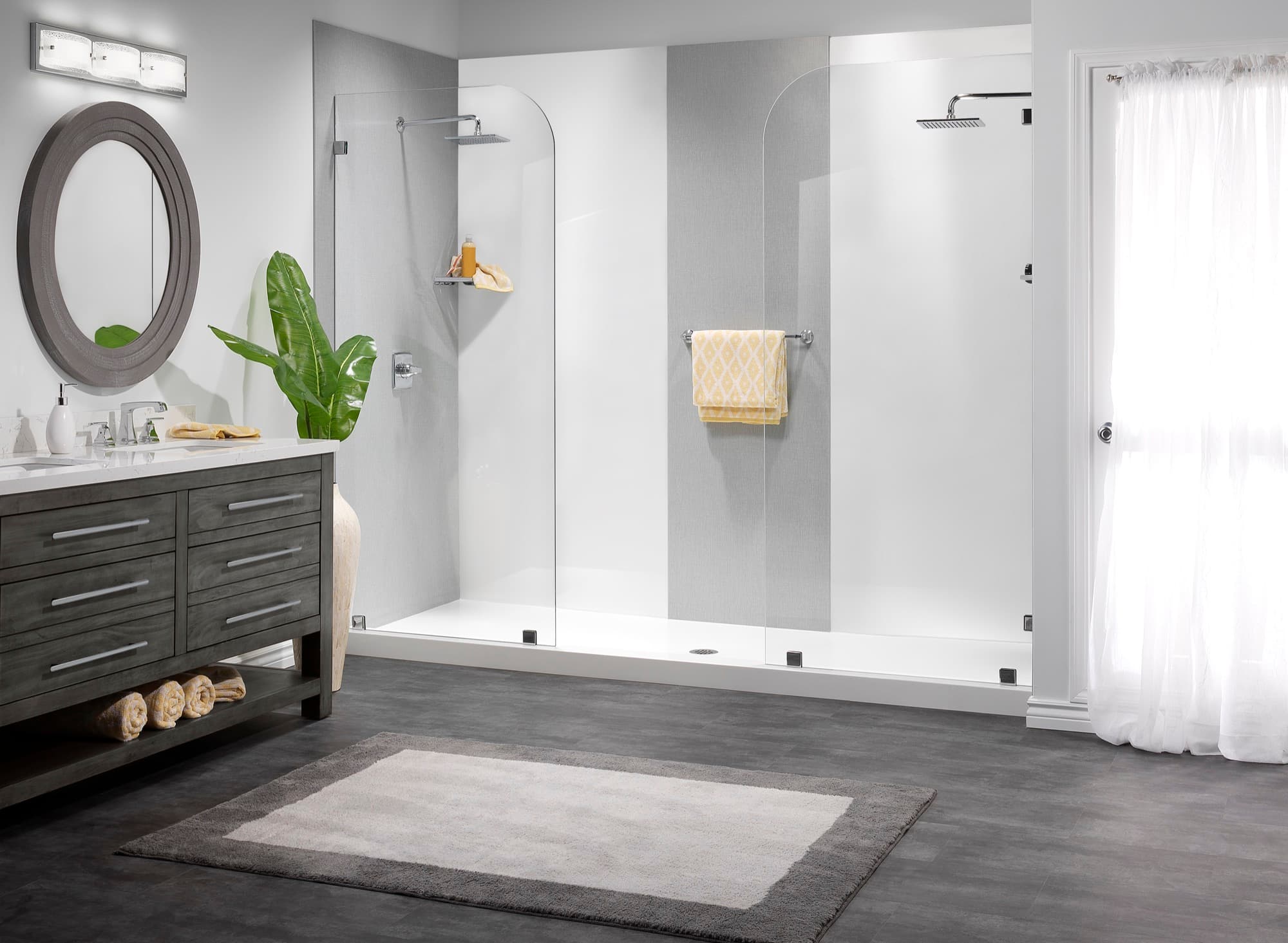 Quiet grey shower walls and clear glass beside a vanity with a round mirror